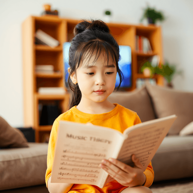 an asian girl reading a music theory book in the living room.png