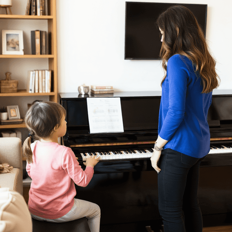 little girl learning piano with a female piano teacher wearing a blue shirt.png